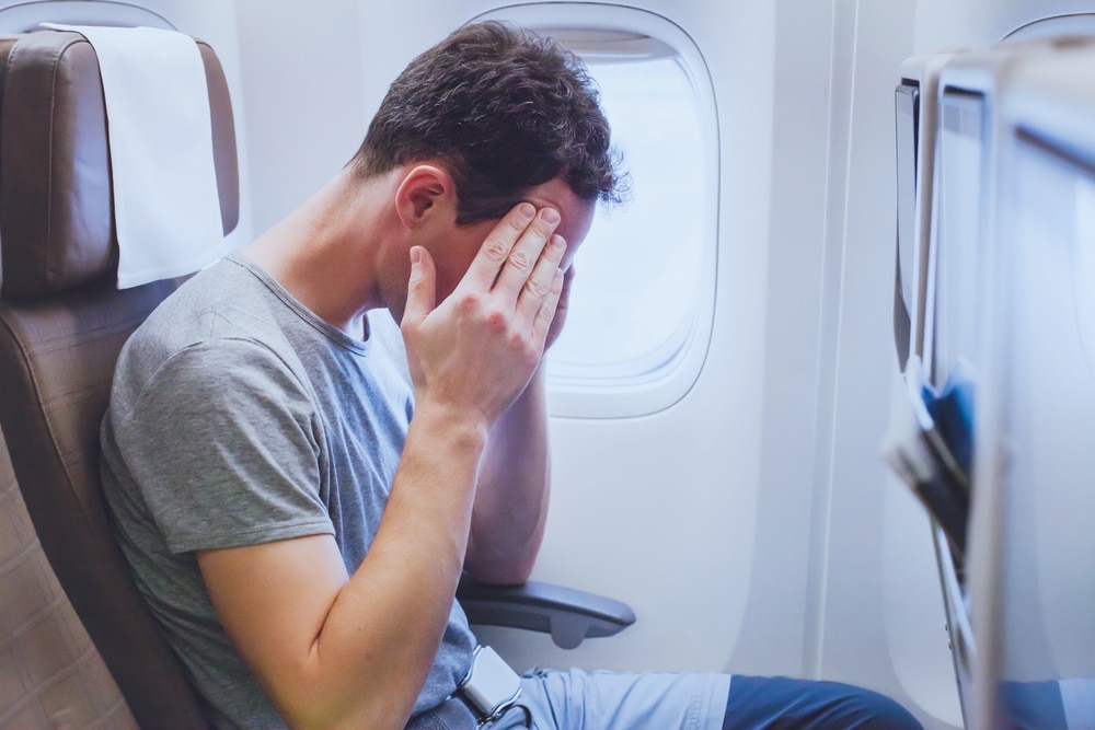 Man on a flight holds his face and sits uncomfortably while trying to ignore his symptoms of dry eye.